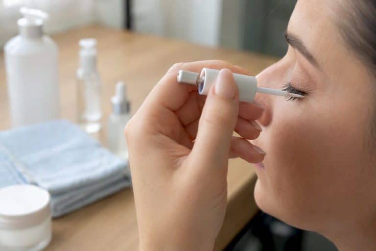 Hand applying eyelash serum to upper lashes